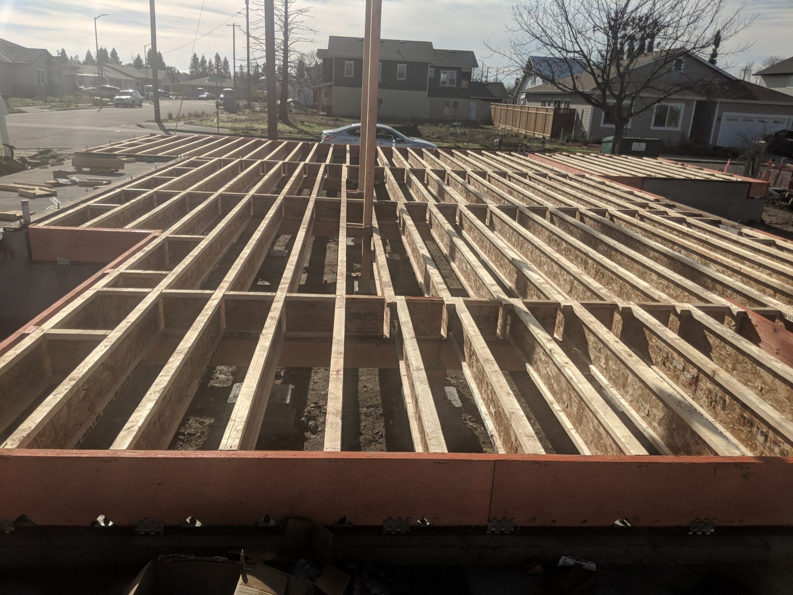 New floor joists on a fresh foundation at the same lot, with neighboring houses under construction.